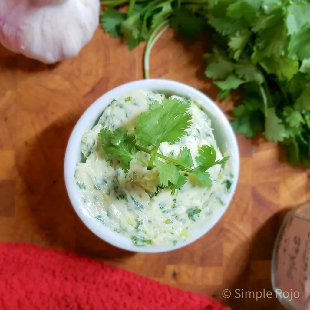 Mantequilla de ajo y cilantro casera en tazón blanco, con textura cremosa y hojas frescas de cilantro, sobre fondo de madera cálido.