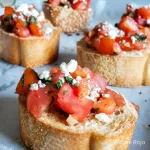 Bruschetta con tomates maduros, queso feta y albahaca fresca sobre pan tostado.