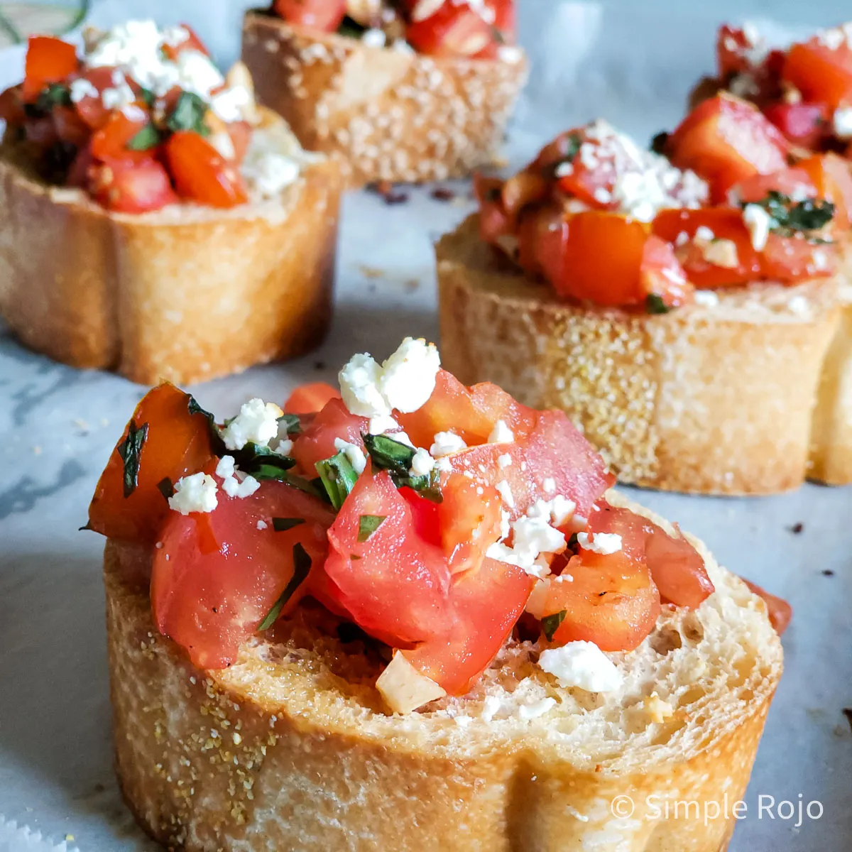 Bruschetta con tomates maduros, queso feta y albahaca fresca sobre pan tostado.